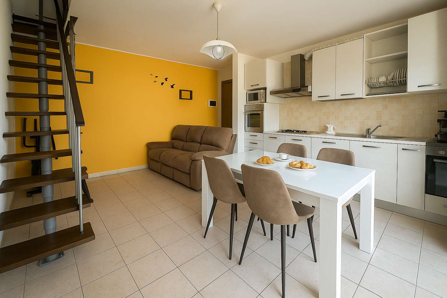Wohnbereich mit Sofa, weißer Küche, Esstisch mit vier Stühlen und Innentreppe