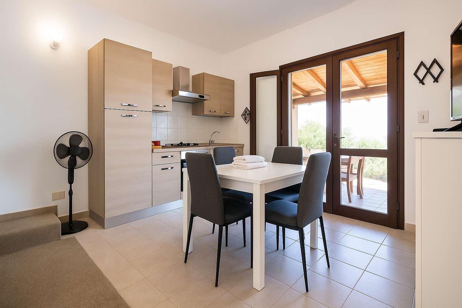 Cucina e zona pranzo con tavolo bianco e sedie grigie, porta-finestra che dà sul portico