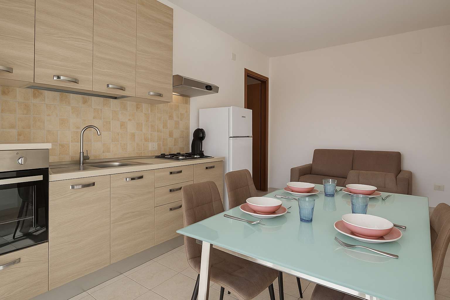 Cuisine avec plaques et four, table à manger dressée et canapé dans le séjour